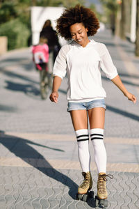 Full length of young woman roller skating on street in city during sunny days