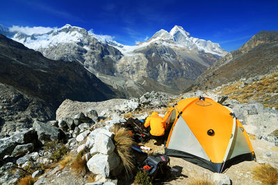 Person crouching by tent on field against mountains