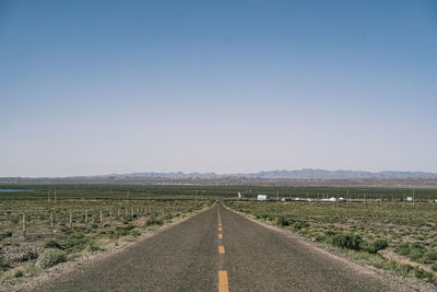 Empty road amidst field against clear sky