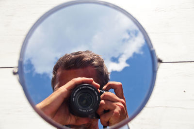 Reflection of man photographing through camera in mirror