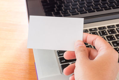 Close-up of woman holding blank paper by laptop on table