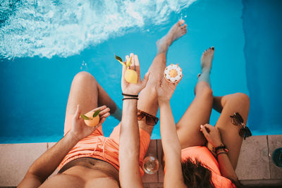 Young man and a girl sit on the edge of a pool and holding fruit