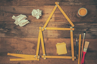 High angle view of rulers in model home shape with painting equipment on wooden table