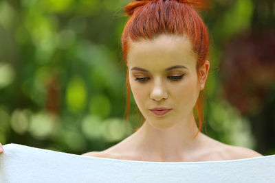Young woman holding towel while looking down against trees