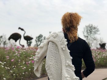 Rear view of woman with sweater standing against sky in park