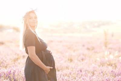 Smiling pregnant woman standing in field on sunny day