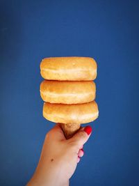 Cropped image of woman holding donuts with ice cream cone against blue background