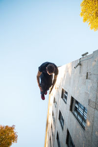 Low angle view of man jumping by buildings against clear sky