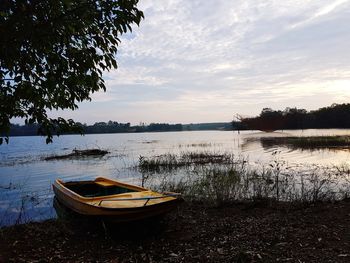 Boat moored at lakeshore against sky during sunset