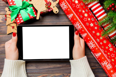 Female hands holding a tablet on christmas background made of fir tree and festive decorations.