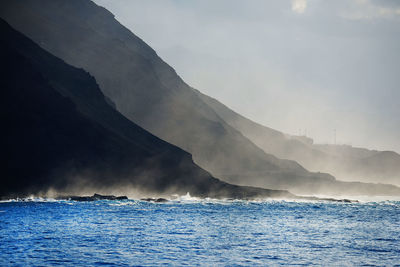 Scenic view of silhouette mountains by sea during foggy weather