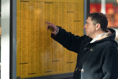 Side view of mature man looking at arrival departure board at station