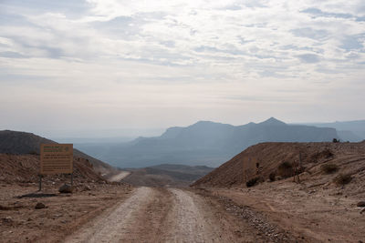 Dirt road leading towards mountains against sky