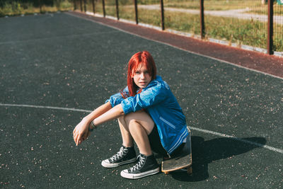 Cute teen girl sitting on a skateboard in the afternoon, outdoors