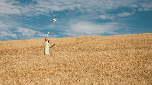 Rear view of woman with arms outstretched on field against sky