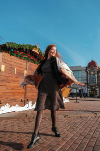 Full length of a smiling young woman standing against building