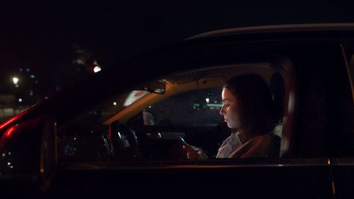 Beautiful business woman using smartphone in a car at night