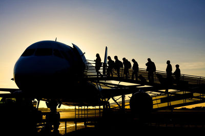 Silhouette people at airport against sky during sunset