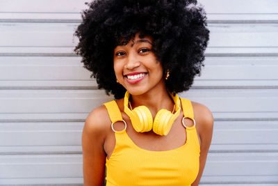 Portrait of young woman with curly hair against wall