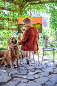 Artist working on her painting outdoors in her garden with golden retriever keeping her company. 