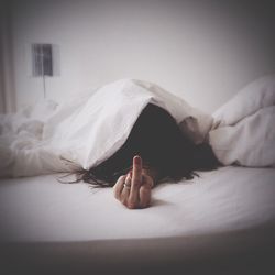 Woman showing middle finger while relaxing on bed