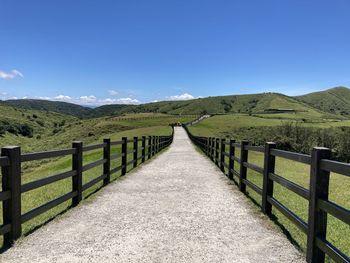 Footpath leading towards mountains against blue sky