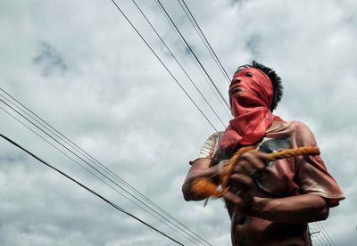 Low angle view of person holding electricity pylon against sky