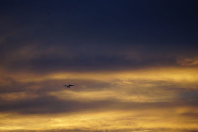 Low angle view of airplane flying against sky during sunset
