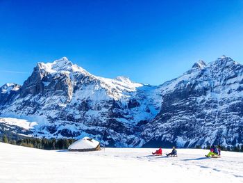 People tobogganing against snowcapped mountains