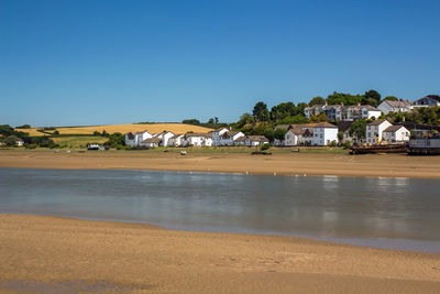 Scenic view of beach by buildings against clear blue sky