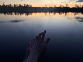 Reflection of hand in lake against sky