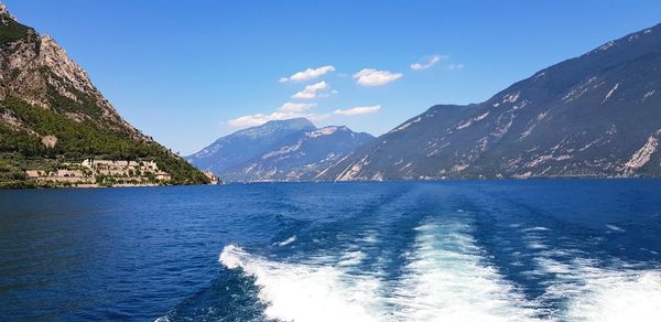 Scenic view of sea by mountains against blue sky