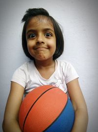 Portrait of cute girl with ball against wall