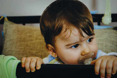 Close-up of cute baby boy with pacifier on bed at home