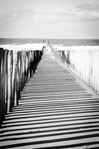 Wooden posts in sea against sky