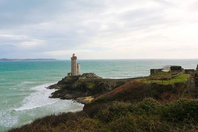 Lighthouse at beach by sea against cloudy sky