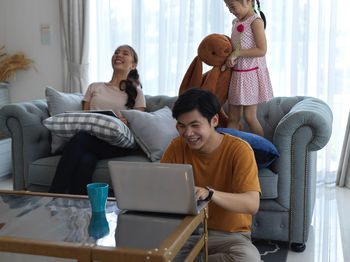 Smiling parents working on laptop while girl playing on sofa at home