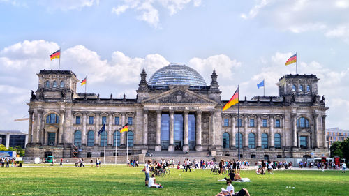 Group of people in front of building against cloudy sky