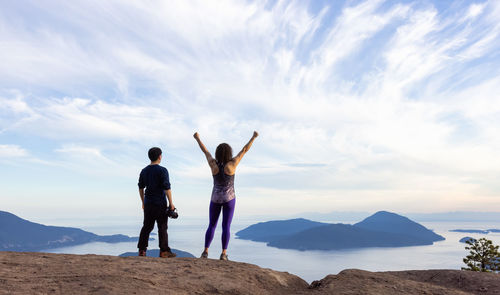 Rear view of friends standing on mountain against sky