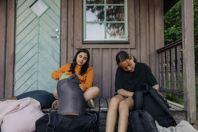 Girls unpacking backpacks while sitting on porch outside cabin