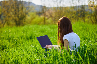 Rear view of woman using mobile phone while sitting on grassy field