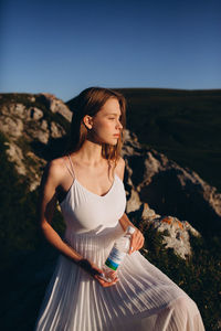 Young woman looking away while standing on rock against sky