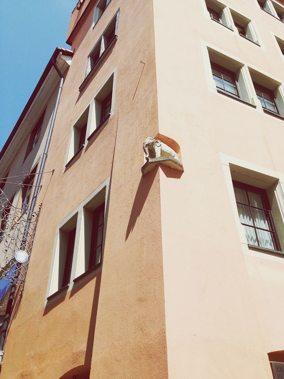 architecture, building exterior, built structure, low angle view, window, building, residential building, city, residential structure, day, outdoors, clear sky, sunlight, human representation, brick wall, no people, shadow, facade, sky, art and craft