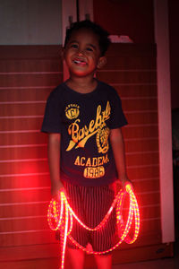 Portrait of smiling girl standing against illuminated wall