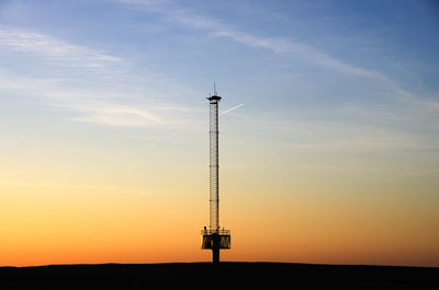 Low angle view of silhouette communications tower against sky during sunset