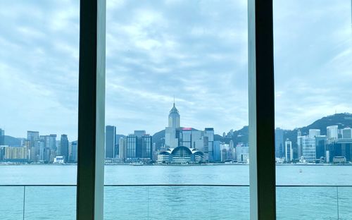 Buildings in city against cloudy sky seen through window