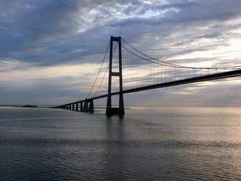 Suspension bridge over sea against cloudy sky