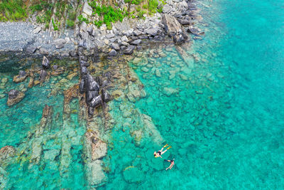 People snorkeling in clear blue water near island rocks