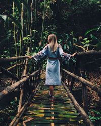 Rear view of young woman standing on footbridge in forest