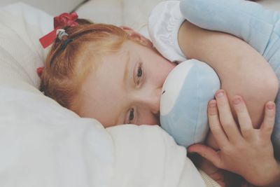Close-up of girl embracing stuffed toy while lying on bed at home